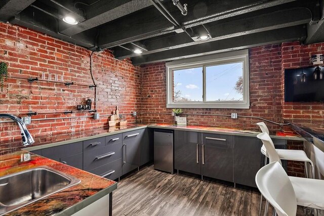 kitchen with brick wall, dark wood-style flooring, a sink, and refrigerator