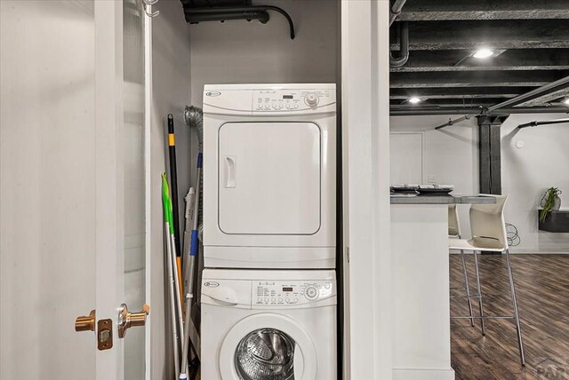 laundry room featuring dark wood-style floors, stacked washer and clothes dryer, and laundry area