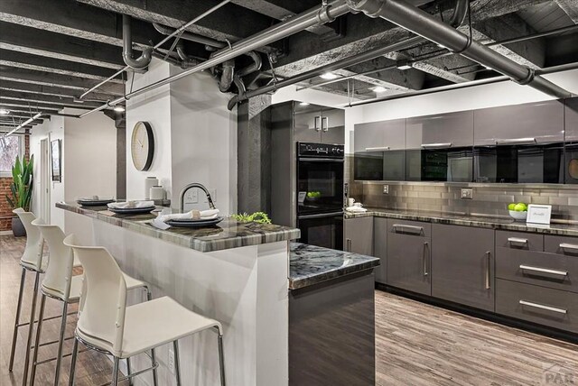 kitchen with a breakfast bar, a center island, dobule oven black, modern cabinets, and light wood-type flooring