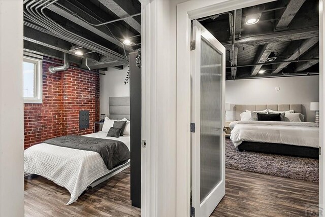 bedroom featuring brick wall and dark wood finished floors