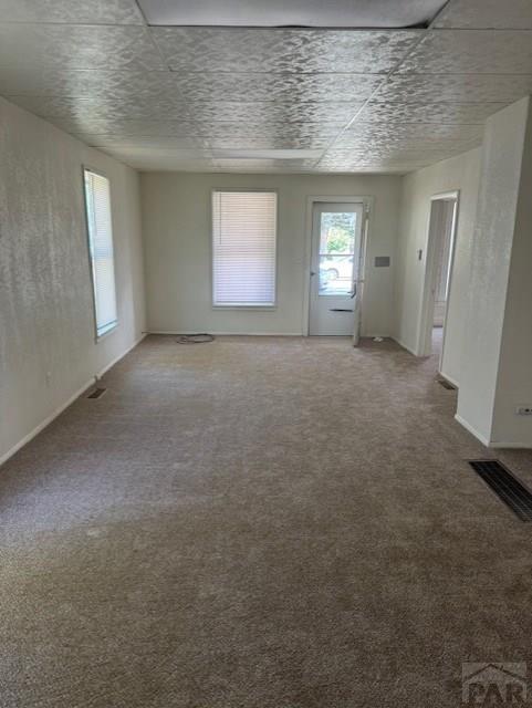 unfurnished living room featuring carpet, visible vents, and a drop ceiling