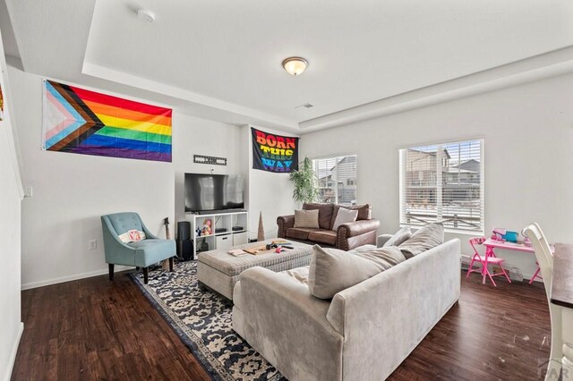 living area featuring dark wood-style floors, a tray ceiling, visible vents, and baseboards