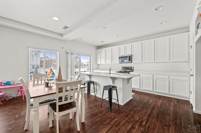 kitchen with light countertops, appliances with stainless steel finishes, a center island with sink, and white cabinets