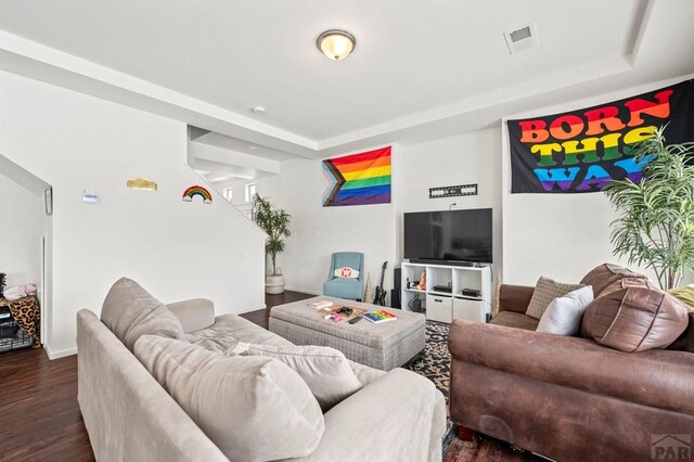 living room featuring baseboards, a tray ceiling, visible vents, and dark wood-style flooring