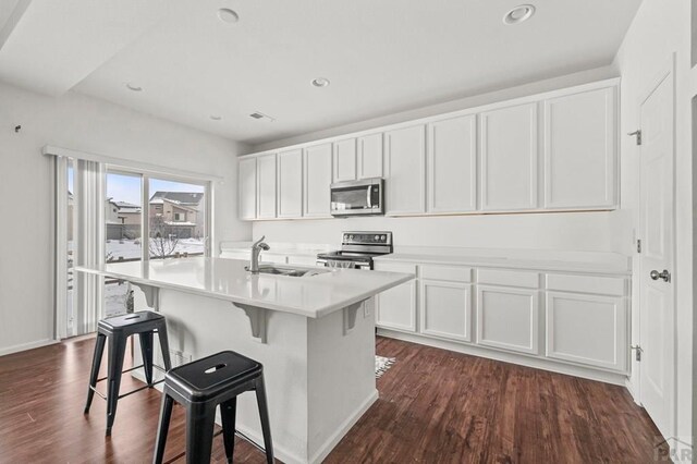 kitchen featuring light countertops, appliances with stainless steel finishes, a kitchen island with sink, a sink, and white cabinetry