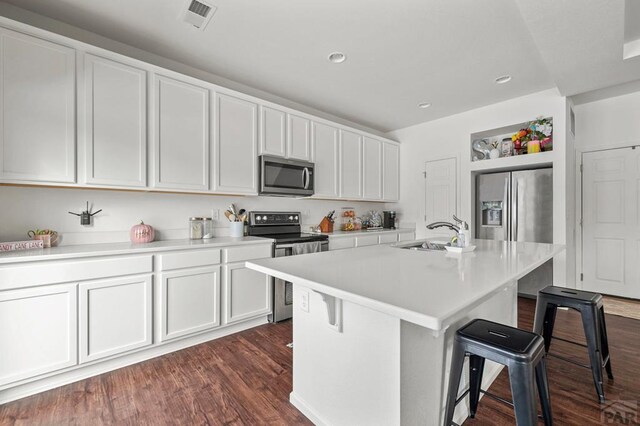 kitchen with a breakfast bar area, a sink, light countertops, appliances with stainless steel finishes, and a center island with sink