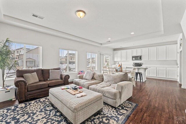 living area with baseboards, visible vents, a raised ceiling, dark wood finished floors, and recessed lighting