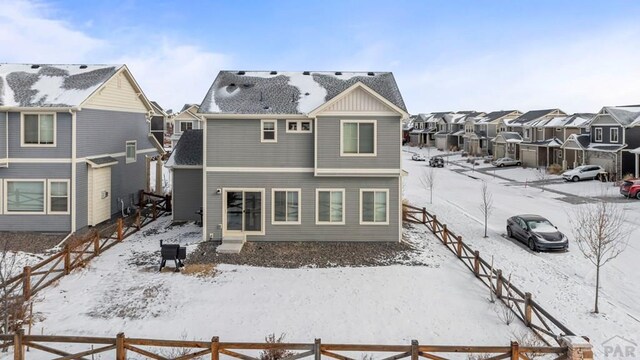 snow covered house with a residential view, fence, and roof with shingles