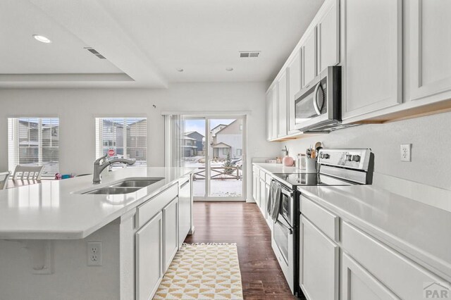 kitchen with stainless steel appliances, light countertops, a kitchen island with sink, a sink, and white cabinetry