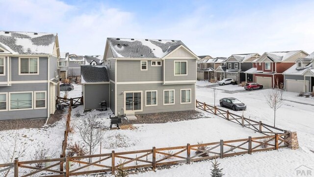 snow covered rear of property featuring a garage, a residential view, and fence