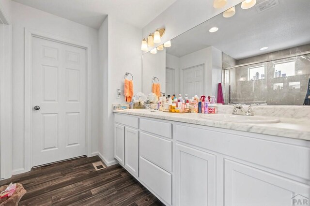 full bathroom featuring double vanity, visible vents, a sink, a shower stall, and wood finished floors