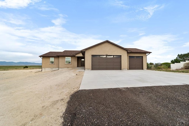 ranch-style home with an attached garage, driveway, a mountain view, and stucco siding