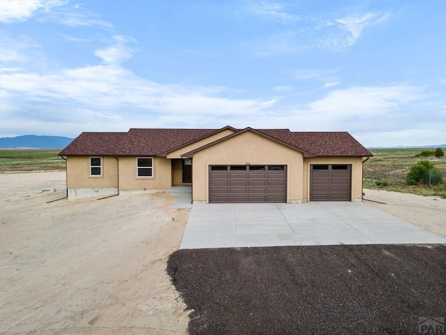 ranch-style home with a garage, driveway, a mountain view, and stucco siding