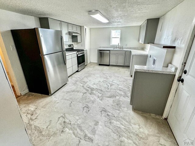 kitchen with appliances with stainless steel finishes, marble finish floor, gray cabinets, light countertops, and under cabinet range hood