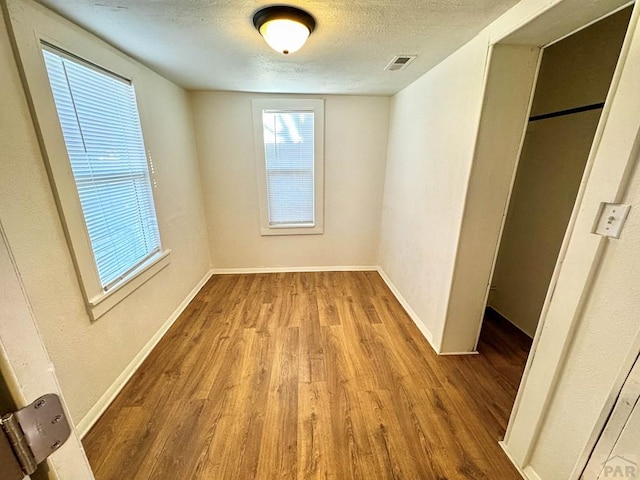 unfurnished bedroom featuring visible vents, a textured ceiling, baseboards, and wood finished floors