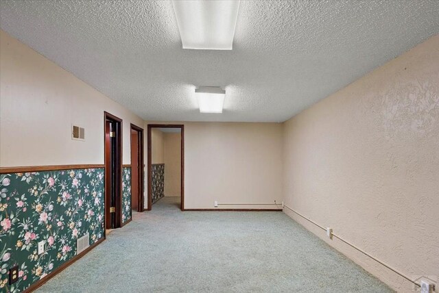 carpeted empty room with a baseboard heating unit, a textured wall, a textured ceiling, and visible vents