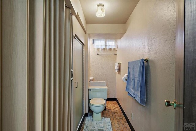 bathroom with a textured wall, an enclosed shower, toilet, and baseboards