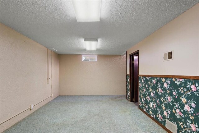 basement with carpet, visible vents, a textured wall, and a textured ceiling