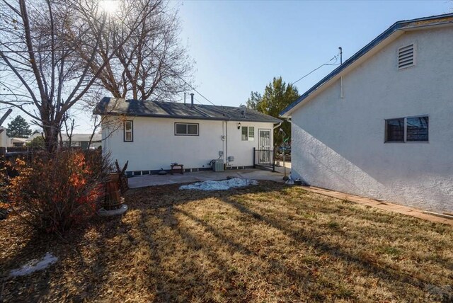 back of property featuring central AC unit, a lawn, and stucco siding