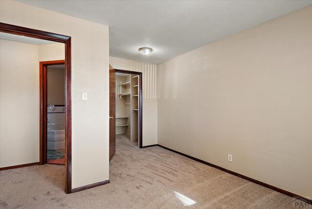 unfurnished bedroom with a walk in closet, light carpet, a textured ceiling, and baseboards