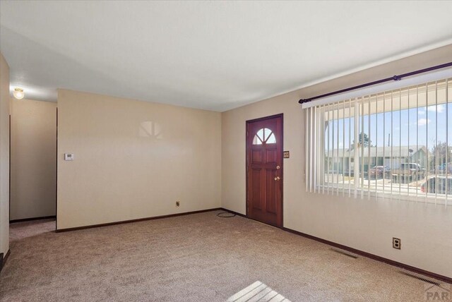 entryway featuring baseboards, visible vents, and light colored carpet