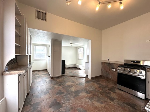 kitchen featuring open shelves, light countertops, visible vents, stone finish floor, and gas range