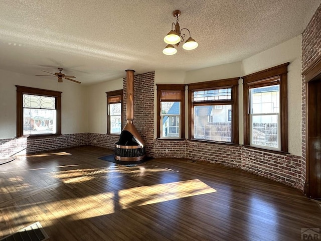 unfurnished living room featuring a textured ceiling, brick wall, dark wood finished floors, and a wood stove