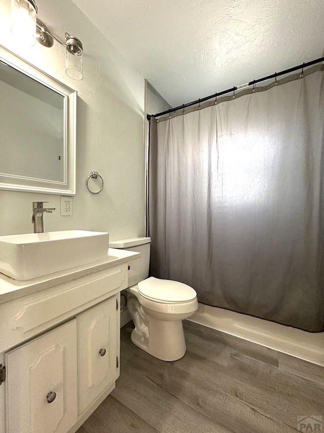 bathroom featuring a textured ceiling, toilet, wood finished floors, vanity, and a shower with curtain