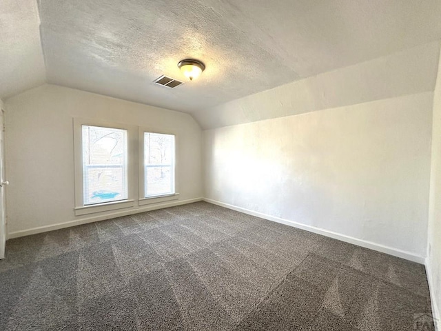 additional living space featuring a textured ceiling, visible vents, baseboards, vaulted ceiling, and dark colored carpet