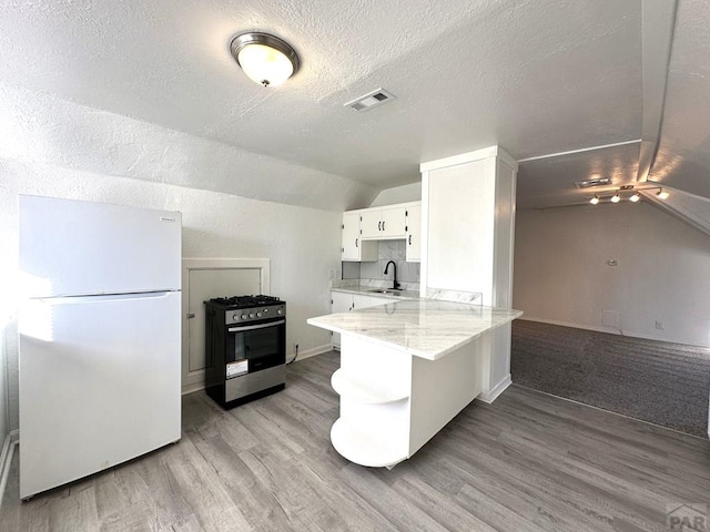 kitchen featuring a peninsula, a sink, white cabinetry, stainless steel gas range, and freestanding refrigerator