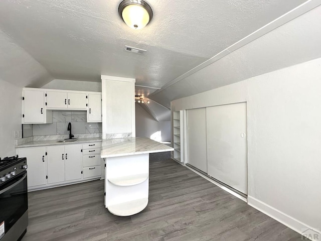 kitchen with lofted ceiling, dark wood-style flooring, white cabinetry, light countertops, and stainless steel range with gas cooktop