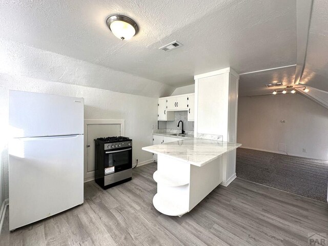 2023 N Elizabeth St, Pueblo, CO 81003 - kitchen with freestanding refrigerator, stainless steel range with gas stovetop, vaulted ceiling, light wood-type flooring, and white cabinetry
