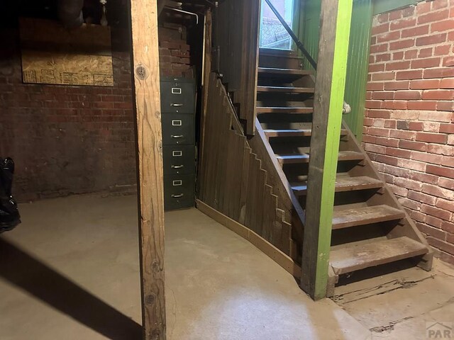 staircase with concrete flooring and brick wall