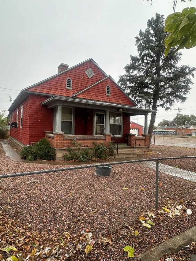 view of front of house with a porch, brick siding, and fence