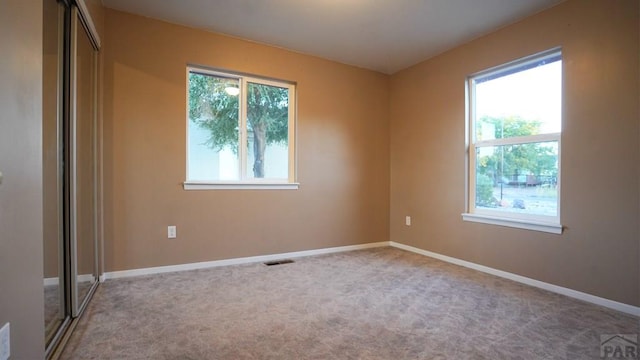 spare room with light carpet, a wealth of natural light, visible vents, and baseboards