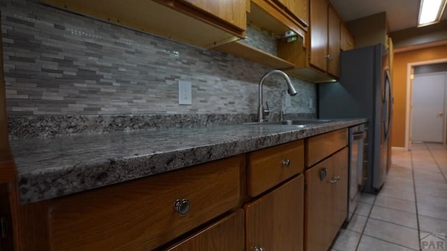 kitchen with light tile patterned floors, a sink, brown cabinets, tasteful backsplash, and dark countertops