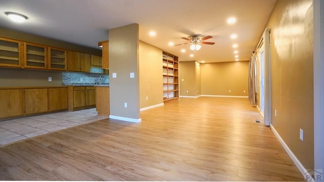 kitchen featuring light wood-style flooring, glass insert cabinets, brown cabinets, light countertops, and a sink