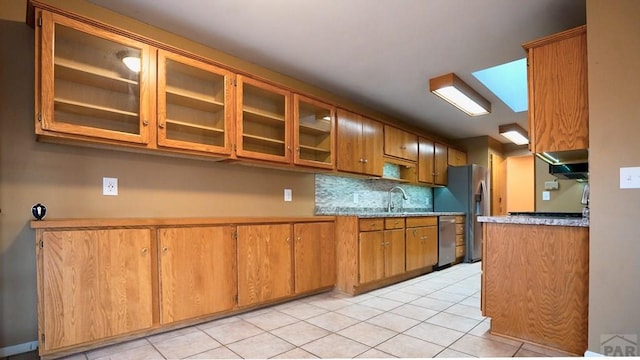 kitchen featuring glass insert cabinets, brown cabinets, stainless steel appliances, and tasteful backsplash