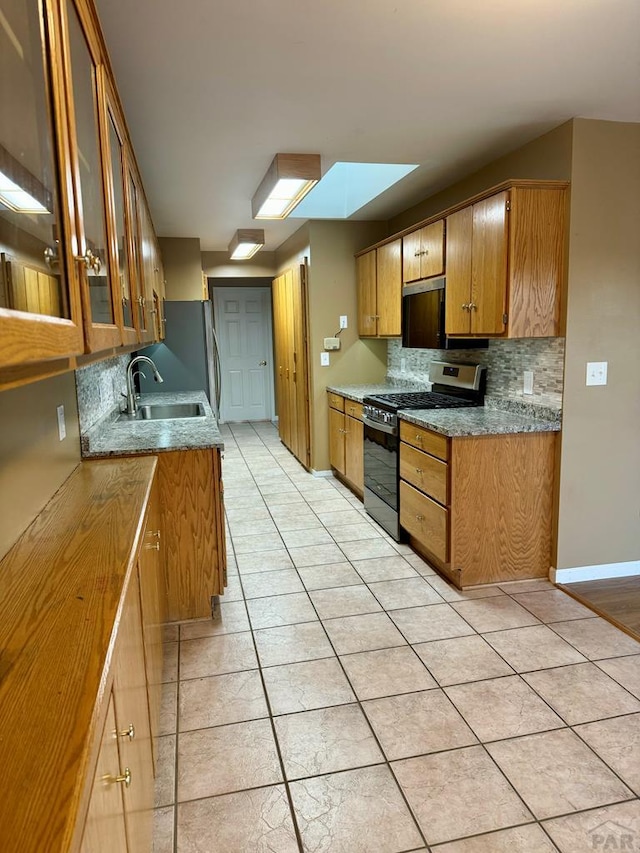 kitchen with stainless steel gas stove, decorative backsplash, glass insert cabinets, brown cabinets, and a sink