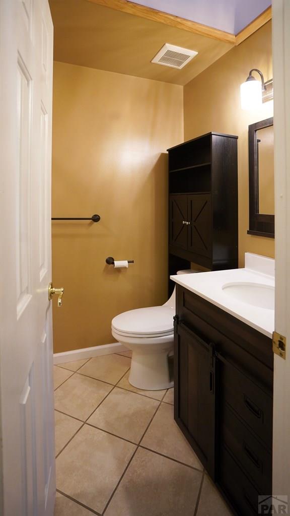 half bathroom featuring visible vents, baseboards, toilet, tile patterned flooring, and vanity