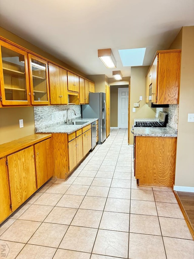 kitchen featuring light tile patterned flooring, stainless steel appliances, a skylight, a sink, and glass insert cabinets