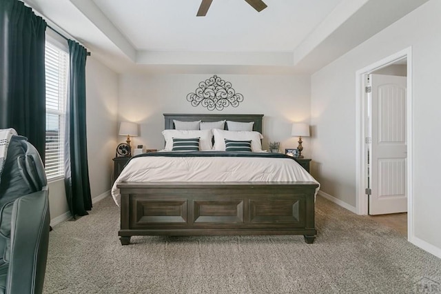 bedroom with light carpet, baseboards, ceiling fan, and a tray ceiling