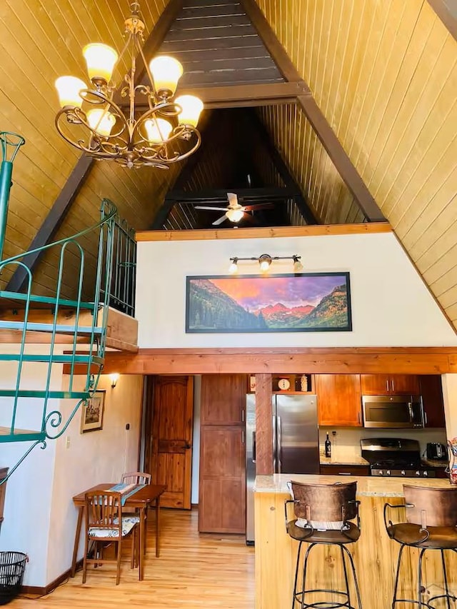 kitchen with appliances with stainless steel finishes, a breakfast bar area, light countertops, light wood-type flooring, and high vaulted ceiling