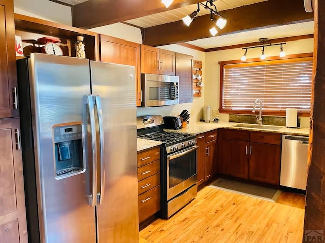 kitchen with light wood-style flooring, a sink, appliances with stainless steel finishes, light stone countertops, and beamed ceiling