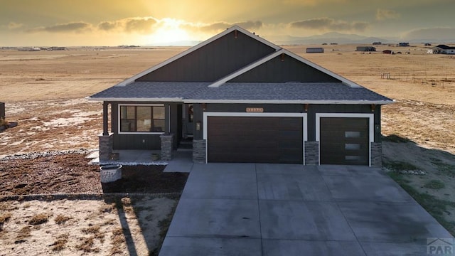 view of front of property with driveway, stone siding, a garage, and roof with shingles