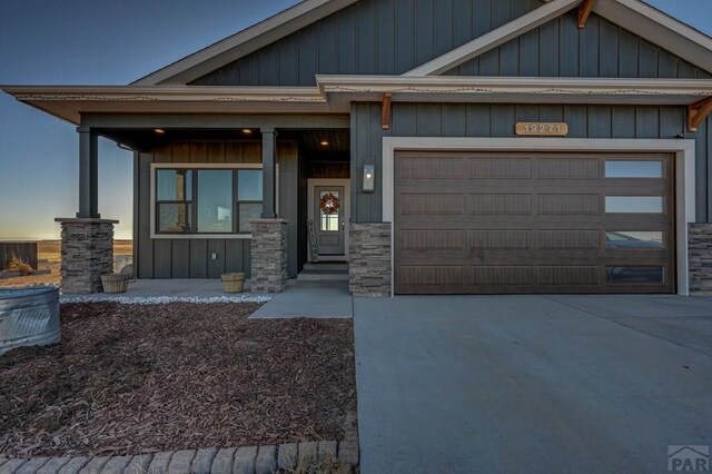 craftsman-style home with a porch, a garage, driveway, stone siding, and board and batten siding