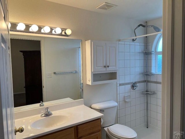 full bath featuring visible vents, a tile shower, vanity, and toilet