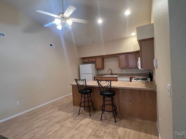 kitchen featuring white appliances, brown cabinetry, a peninsula, light countertops, and a sink