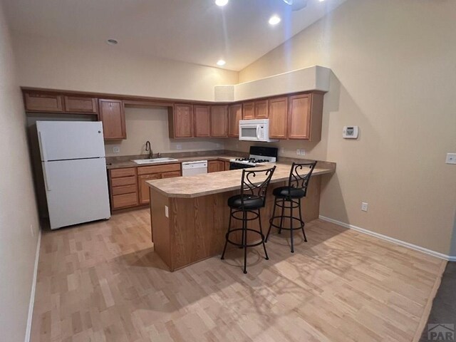 kitchen with brown cabinets, light countertops, a sink, white appliances, and a peninsula