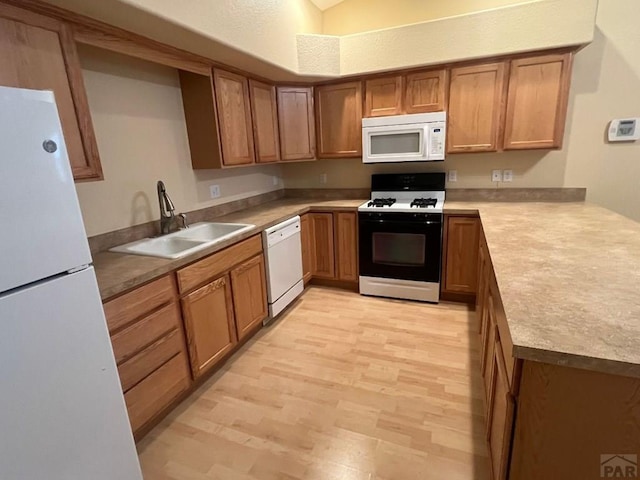 kitchen with white appliances, brown cabinetry, light countertops, light wood-type flooring, and a sink